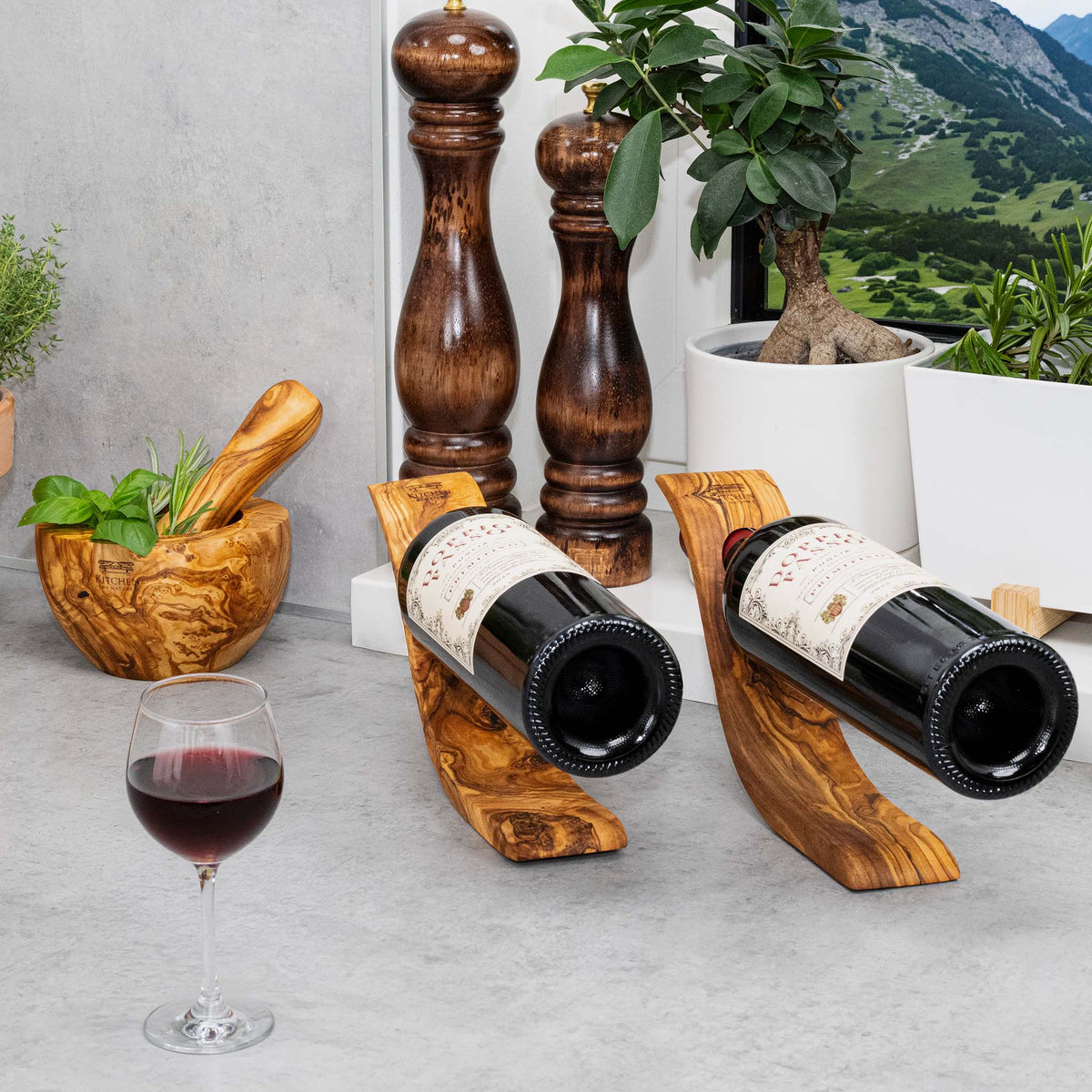 Dos botelleros de madera de olivo en la cocina junto a un mortero de madera y molinillos de pimienta